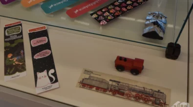 W szklanej gablocie zaprezentowane są drobne przedmioty artystyczne i użytkowe, w tym zakładki do książek, niewielkie figurki oraz elementy rękodzielnicze. Zdjęcie ukazuje fragment wystawy „Pomiędzy stronami” prezentowanej w Mediatece 800-lecia.