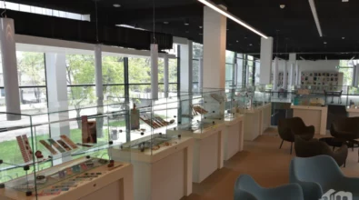 W jasnej przestrzeni Mediateki 800-lecia ustawiony jest długi ciąg szklanych gablot ekspozycyjnych z pracami artystycznymi, rozmieszczonych wzdłuż przeszklonej ściany z widokiem na zieleń na zewnątrz. Zdjęcie ukazuje ogólny widok wystawy „Pomiędzy stronami”.