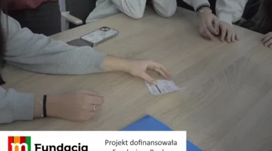 Zdjęcie przedstawia uczestników warsztatów edukacyjnych siedzących przy stole i wspólnie analizujących kartę z zadaniem, podczas zajęć realizowanych w ramach projektu dofinansowanego przez Fundację mBanku.