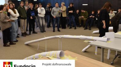 Uczestnicy obserwują testy dużej papierowej konstrukcji. Na dole logotyp Fundacji mBanku.