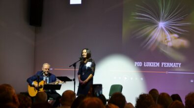 Kobieta śpiewa na scenie, mężczyzna obok gra na gitarze.