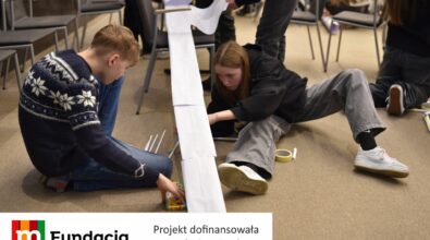Dwoje uczestników konstruuje długą papierową konstrukcję. Na dole logotyp Fundacji mBanku.
