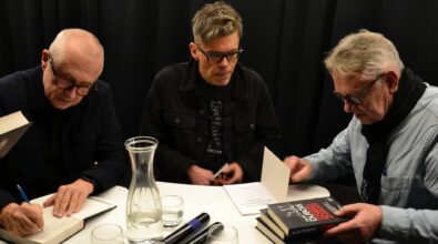 Trzy osoby siedzą przy stole podczas spotkania autorskiego, podpisują książki.