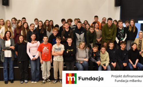 Grupa około pięćdziesięciu młodych uczestników wraz z opiekunami pozuje wspólnie do fotografii. Na dole logotyp Fundacji mBanku.