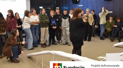 Uczestnicy wydarzenia zgromadzili się wokół prowadzącej, słuchując jej wystąpienia. Na dole logotyp Fundacji mBanku.