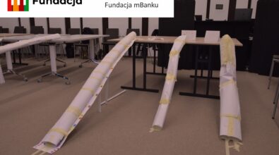 Na stołach i podłodze ustawiono papierowe konstrukcje z zakrętami i spadkami. Na górze logotyp Fundacji mBanku.