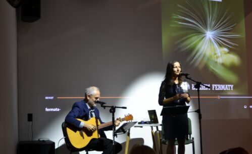 Kobieta śpiewa na scenie, mężczyzna obok gra na gitarze.