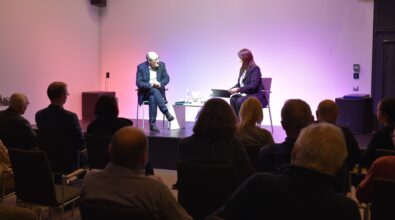 Błażej Torański i prowadząca spotkanie siedzą na scenie, publiczność obserwuje.