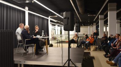 Zdjęcie ze spotkania. Na scenie goście wraz z prowadzącym. Przed scena uczestnicy.