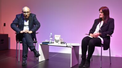 Błażej Torański i prowadząca spotkanie siedzą na scenie i rozmawiają przy niskim białym stoliku.