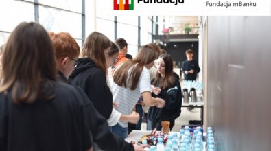 Uczestnicy wydarzenia gromadzą się przy stole z przekąskami i napojami. Na górze logotyp Fundacji mBanku.