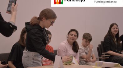 Uczestnicy konstruują model z papieru i taśmy, a na stole widoczny jest zabawkowy samochód. Na górze logotyp Fundacji mBanku.