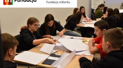 Uczniowie pracują wspólnie nad zadaniem edukacyjnym, korzystając z papieru, kleju i przyborów szkolnych . Na górze logotyp Fundacji mBanku.