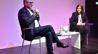 Błażej Torański i prowadząca spotkanie siedzą na scenie przy niskim białym stoliku.