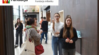 Grupa młodych ludzi rozmawia i integruje się w jasnym wnętrzu. Na górze logotyp Fundacji mBanku.