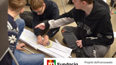 Młodzi uczestnicy wspólnie budują papierową konstrukcję, wykorzystując taśmę i rurki. Na dole logotyp Fundacji mBanku.