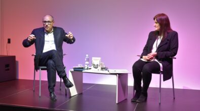 Błażej Torański i prowadząca spotkanie siedzą na scenie i rozmawiają przy niskim białym stoliku.