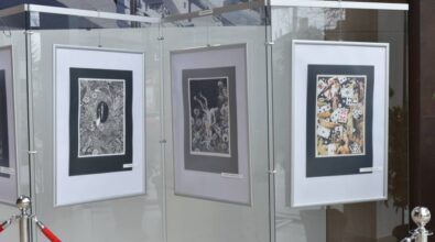 Na ścianie ekspozycyjnej zawieszone są trzy oprawione prace artystyczne o zróżnicowanej kolorystyce i formie, umieszczone obok siebie w równym układzie. Zdjęcie przedstawia fragment wystawy prezentowanej w przestrzeni Miejskiej Biblioteki Publicznej.