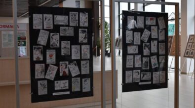 Na dwóch czarnych planszach ekspozycyjnych zawieszone są liczne rysunki i grafiki w jasnych tonacjach, ułożone w regularnych odstępach. Zdjęcie przedstawia fragment wystawy artystycznej prezentowanej w przestrzeni Miejskiej Biblioteki Publicznej.