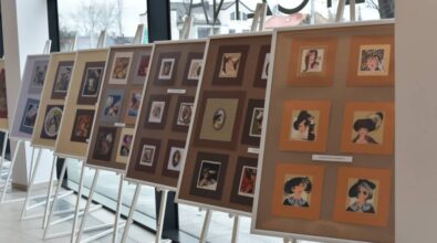 Na sztalugach ustawione są plansze ekspozycyjne z oprawionymi pracami artystycznymi przedstawiającymi portrety i ilustracje, rozmieszczone w kilku rzędach. Zdjęcie ukazuje fragment wystawy prezentowanej w przestrzeni Miejskiej Biblioteki Publicznej.