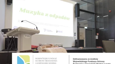 Na zdjęciu widoczna jest sala Mediateki z przygotowaną sceną i mównicą, przed którą wyświetlana jest prezentacja zatytułowana „Muzyka z odpadów” realizowana w ramach projektu EkoTEKA. Na dole kadru znajdują się instrumenty edukacyjne oraz informacja o dofinansowaniu zadania ze środków Wojewódzkiego Funduszu Ochrony Środowiska i Gospodarki Wodnej w Łodzi.