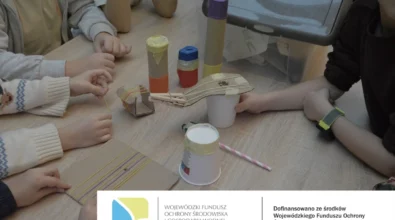 Na zdjęciu widoczne są dzieci pracujące przy stole podczas warsztatów edukacyjnych, tworzące proste instrumenty muzyczne z materiałów z recyklingu, takich jak tekturowe tuby, kubki papierowe, gumki recepturki i patyczki. Zajęcia odbywają się w ramach projektu EkoTEKA i mają na celu rozwijanie kreatywności oraz kształtowanie postaw proekologicznych poprzez praktyczne działania. Warsztaty zostały dofinansowane ze środków Wojewódzkiego Funduszu Ochrony Środowiska i Gospodarki Wodnej w Łodzi.