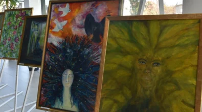 Na sztalugach ustawione są obrazy malarskie o intensywnej kolorystyce, przedstawiające symboliczne kobiece twarze i fantastyczne formy inspirowane naturą. Zdjęcie ukazuje fragment wystawy malarstwa Joanny Prus prezentowanej w przestrzeni Mediateki 800-lecia.