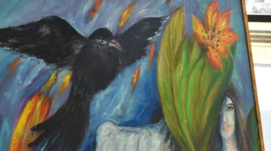 Fragment obrazu malarskiego przedstawiający czarnego ptaka z rozpostartymi skrzydłami na tle intensywnie kolorowanej, symbolicznej kompozycji z motywami roślinnymi i kobiecą twarzą. Zdjęcie ukazuje detal jednego z obrazów prezentowanych na wystawie malarstwa Joanny Prus w Mediatece 800-lecia.