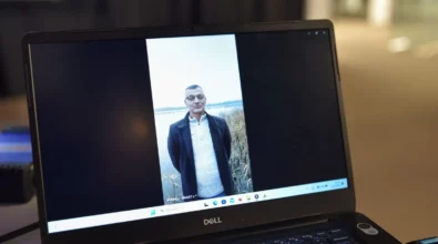 Na ekranie laptopa wyświetlany jest film przedstawiający mężczyznę stojącego nad brzegiem jeziora. Nagranie odtwarzane jest podczas wydarzenia odbywającego się w Mediatece, a komputer ustawiony jest na stole w przestrzeni przygotowanej do prezentacji materiałów multimedialnych.