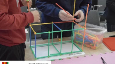 Dzieci budują przestrzenną konstrukcję z kolorowych rurek i łączników, tworząc geometryczny szkielet przypominający model budynku. Uczestnicy wspólnie dopasowują elementy i stabilizują kolejne części konstrukcji, rozwijając wyobraźnię przestrzenną, umiejętność współpracy oraz podstawy myślenia technicznego podczas zajęć w Mediatece 800-lecia realizowanych w ramach projektu „MatSensoryka 4”, dofinansowanego przez Fundację mBanku.