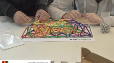 Uczestnicy warsztatów budują konstrukcję z kolorowych patyczków i metalowych kulek magnetycznych. Na macie edukacyjnej powstaje przestrzenna struktura złożona z wielu trójkątów, rozwijająca wyobraźnię przestrzenną i umiejętność logicznego myślenia. Zajęcia odbywają się w ramach projektu „MatSensoryka 4”, dofinansowanego przez Fundację mBanku.