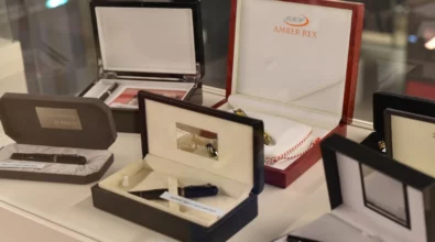 Elegancka gablotka z kolekcją ekskluzywnych piór wiecznych i długopisów zaprezentowanych w ozdobnych etui. Na pierwszym planie czarne i granatowe modele w aksamitnych pudełkach, a w tle eleganckie zestawy w drewnianych kasetkach, w tym Amber Rex. Wystawa podkreśla prestiż i kunszt piśmienniczych akcesoriów.