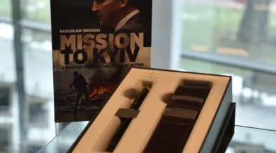 W gablocie wystawowej znajduje się pióro wieczne w eleganckim etui oraz książka „Mission to Kyiv” z wizerunkiem autora na okładce. Zdjęcie przedstawia fragment wystawy „Historia i teraźniejszość Polski – piórem wiecznym pokazana” prezentowanej w Miejskiej Bibliotece Publicznej im. Adama Próchnika.