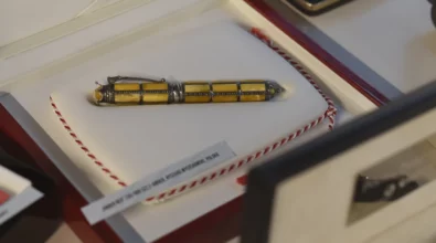 W gablocie wystawowej zaprezentowane jest pióro wieczne o dekoracyjnym wykończeniu, umieszczone w jasnym etui i opatrzone opisem informacyjnym. Zdjęcie przedstawia fragment wystawy „Historia i teraźniejszość Polski – piórem wiecznym pokazana” prezentowanej w Miejskiej Bibliotece Publicznej im. Adama Próchnika.