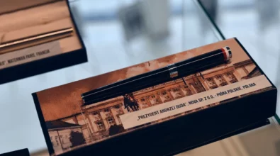 W gablocie wystawowej wyeksponowane jest pióro wieczne umieszczone w etui z motywem architektonicznym, opatrzone opisem informacyjnym. Zdjęcie przedstawia fragment wystawy „Historia i teraźniejszość Polski – piórem wiecznym pokazana” prezentowanej w Miejskiej Bibliotece Publicznej im. Adama Próchnika.