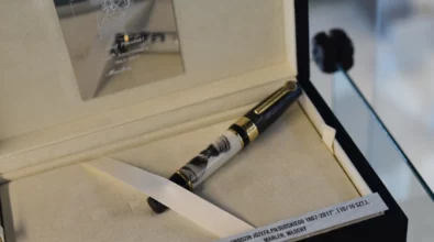 W gablocie wystawowej zaprezentowane jest pióro wieczne umieszczone w jasnym etui, opatrzone etykietą informacyjną. Zdjęcie przedstawia fragment wystawy „Historia i teraźniejszość Polski – piórem wiecznym pokazana” prezentowanej w Miejskiej Bibliotece Publicznej im. Adama Próchnika.