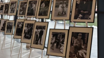 Na sztalugach ustawionych w kilku rzędach prezentowane są oprawione czarno-białe fotografie ukazujące ludzi w codziennych sytuacjach i scenach miejskich. Zdjęcie przedstawia fragment wystawy fotograficznej prezentowanej w przestrzeni Miejskiej Biblioteki Publicznej.