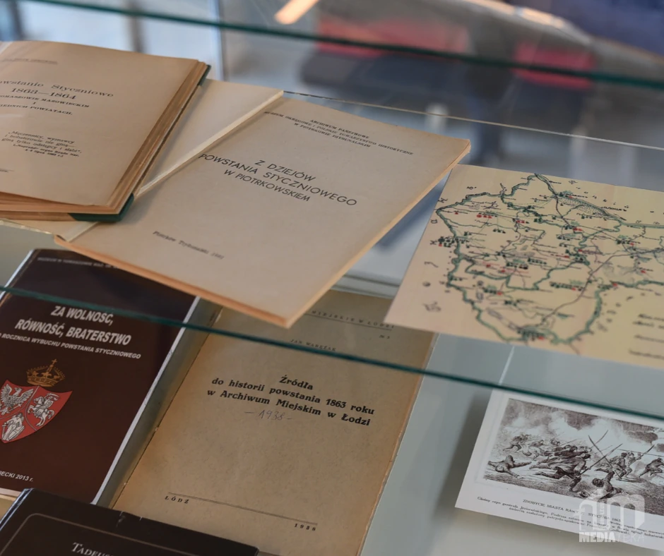 W szklanej gablocie wystawowej ułożone są archiwalne książki, broszury i materiały kartograficzne związane z historią XIX wieku. Zdjęcie przedstawia fragment wystawy historycznej prezentowanej w Miejskiej Bibliotece Publicznej im. Adama Próchnika.