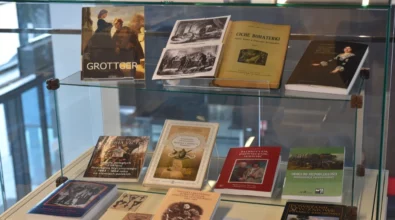 W szklanej gablocie ekspozycyjnej zaprezentowane są książki, albumy i publikacje historyczne o różnorodnej tematyce, ułożone na kilku poziomach. Zdjęcie przedstawia fragment wystawy historycznej prezentowanej w przestrzeni Miejskiej Biblioteki Publicznej.