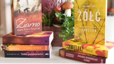 Na zdjęciu widoczne są stosy książek ustawione na stole, z wyeksponowanymi okładkami w ciepłych, jesiennych barwach. W tle znajduje się dekoracja z roślin, wrzosu, jabłka i grzyba, tworząca naturalną, biblioteczną aranżację. Na dole grafiki umieszczono logotypy Narodowego Programu Rozwoju Czytelnictwa 2.0, Ministerstwa Kultury i Dziedzictwa Narodowego oraz Biblioteki Narodowej. Zdjęcie promuje nowości wydawnicze zakupione w ramach programu wspierającego rozwój czytelnictwa.