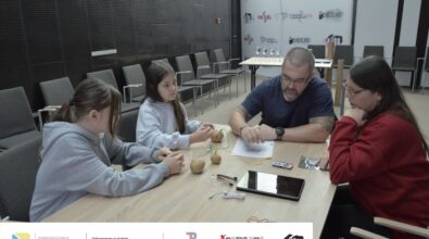 Zdjęcie przedstawia dwie dziewczynki, kobietę oraz mężczyznę siedzących przy stole. Na stole leży tablet, trzy ziemniaki z podłączonymi do nich kolorowymi przewodami oraz inne elementy elektroniczne. Mężczyzna przygląda się jakiejś kartce, prawdopodobnie czyta instrukcję. Z tyłu ściana z napisami Biblioteka, Piotrków Trybunalski i Piksel. Zdjęcie MBP