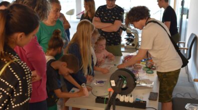 Na zdjęciu widać grupę ludzi stojących przy stoliku. Po jego drugiej stronie znajduje się dwóch nastolatków. Na stoliku znajdują się długopisy 3D, których dzieci używają do tworzenia rysunków, rodzice ich nadzorują. Zdjęcie: MBP.