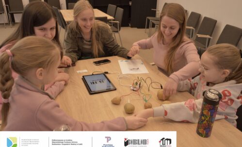 Zdjęcie przedstawia dwie dziewczynki i trzy kobiety siedzące przy stole. Wszystkie osoby trzymają się za ręce i się uśmiechają. Na stole leżą ziemniaki połączone kolorowymi przewodami z płytką elektroniczną i tabletem. Na tablecie wyświetla się klawiatura pianina. Obok leży instrukcja. Zdjęcie MBP.