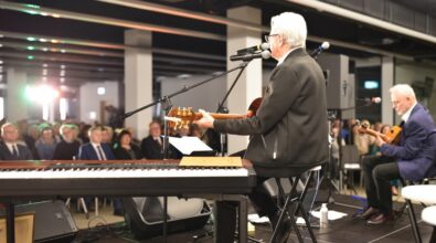 Na zdjęciu widać koncert w przestrzeni Mediateki, ujęty z perspektywy sceny. Na pierwszym planie siedzi starszy mężczyzna grający na gitarze i śpiewający do mikrofonu; przed nim znajduje się klawiatura elektroniczna ustawiona na statywie. Po prawej stronie sceny drugi muzyk, również siedzący, gra na gitarze akustycznej. Scena wyposażona jest w mikrofony, statywy, nagłośnienie i przewody. W tle, naprzeciw wykonawców, widoczna jest licznie zgromadzona publiczność siedząca na krzesłach, skupiona na występie. Zdjęcie oddaje atmosferę kameralnego koncertu i bezpośredni kontakt artystów z odbiorcami.