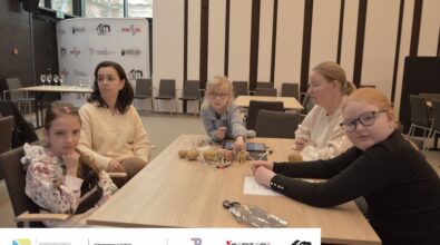 Zdjęcie przedstawia trzy dziewczynki i dwie kobiety siedzące przy stole. Na stole leżą ziemniaki połączone kolorowymi przewodami z płytką elektroniczną i tabletem. Z tyłu ściana z napisami Biblioteka, Piotrków Trybunalski i Piksel. Zdjęcie MBP