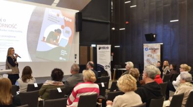 Zdjęcie siedzącej publiczności, w tle kobieta przemawia do mikrofonu, na ekranie prezentacja.