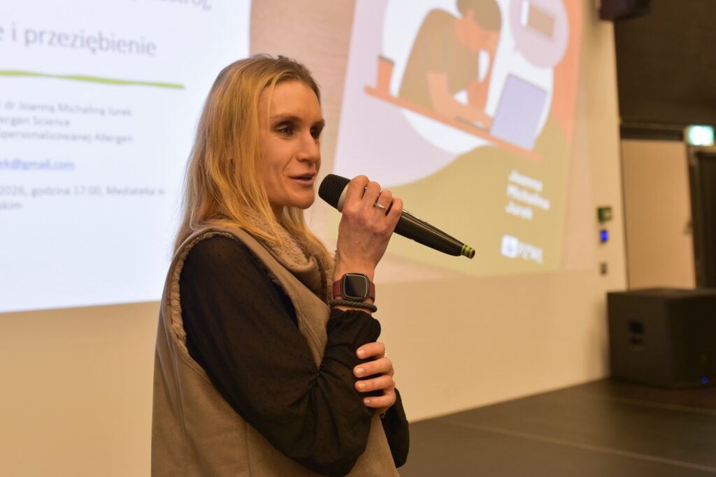 Kobieta przemawiająca do mikrofonu podczas prezentacji, w tle slajd z tekstem po polsku.