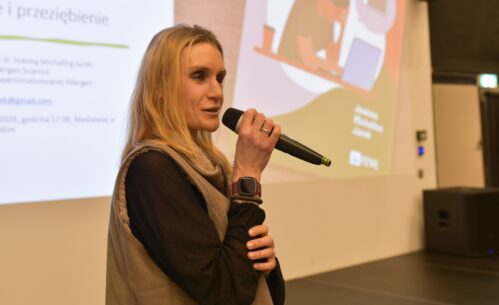 Kobieta przemawiająca do mikrofonu podczas prezentacji, w tle slajd z tekstem po polsku.