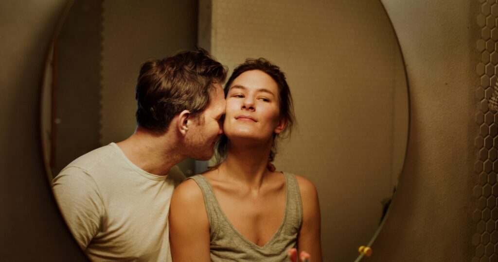 Plakat filmu „Być kochaną” przedstawiający zbliżenie dwojga dorosłych, gdzie mężczyzna pochyla się w stronę kobiety, a ona patrzy przed siebie z zamyślonym wyrazem twarzy. Na grafice widoczne są informacje o projekcji w Kinie Piksel w Mediatece 800-lecia, data 7 lutego 2026 roku, godzina 17:00 oraz oznaczenie wiekowe 15+.