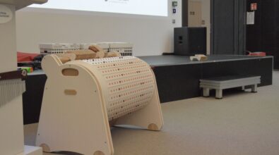 Na zdjęciu widać drewniane urządzenie z przyciskami. Za nim znajduje się podwyższenie, prawdopodobnie scena. Widać również fragment wyświetlanej prezentacji. Drzwi do pomieszczenia są otwarte. Zdjęcie: MBP.